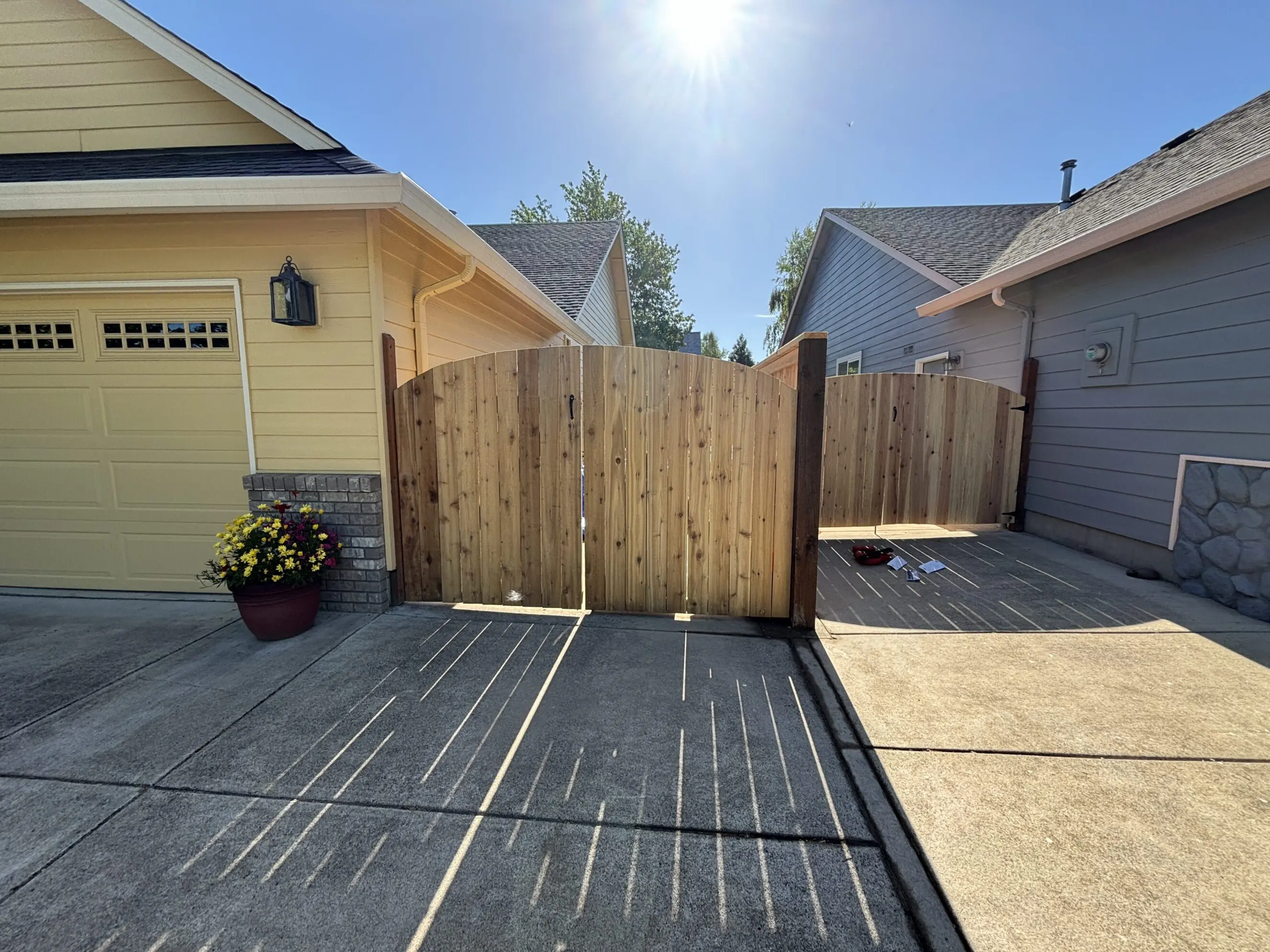 wooden double gate fence installed between a yellow garage and a gray house on a sunny day, showcasing quality craftsmanship and curb appeal by Timberhill Fence & Deck